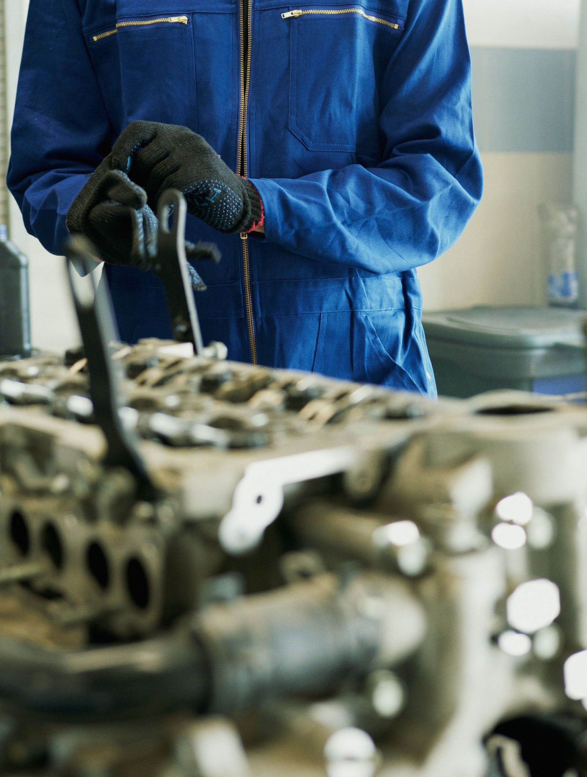 Mechanic wearing blue coveralls and gloves inspecting an engine in a workshop.